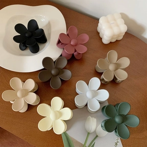 Matte flower hair claw clips in various Morandi colors on a warm wooden surface