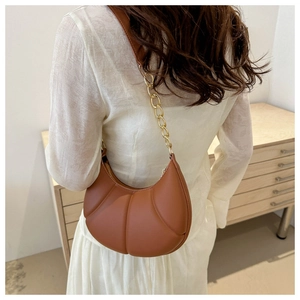 Brown pleated crescent shoulder bag with gold chain strap shown on white dress