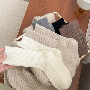Vertical ribbed knit crew socks in neutral tones arranged in a rustic wicker basket
