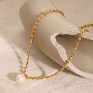 Collier élégant en or avec pendentif perle exposé sur un support en céramique
