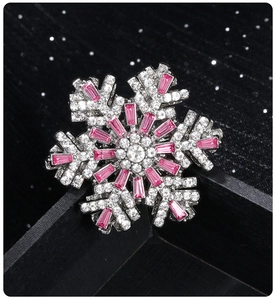 Close-up of a rotating snowflake brooch with pink and clear rhinestones on a black background