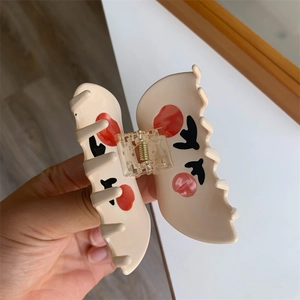 Close-up of a cream floral hair claw clip with artistic red and black patterns