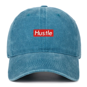 Detailed embroidery of white Hustle text on red patch on washed blue cotton baseball cap