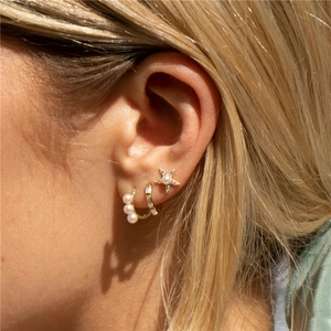 Macro shot of gold star pearl earring and zircon hoop set on model's ear