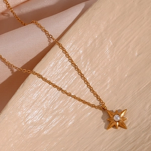 Detailansicht eines goldenen Achtzackstern-Anhängers mit Perle an einer feinen Halskette