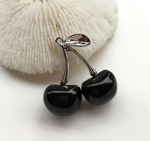 Detailed close-up of glossy black cherry pendant with silver leaves on coral background