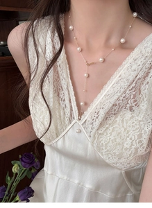 Detail view of a French vintage pearl Y-necklace worn with a white lace silk dress