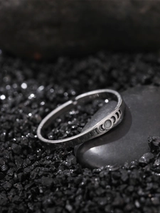 Macro shot of silver lunar phase engraved ring placed on a dark stone background