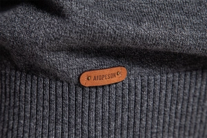 Macro view of dark grey knitted sweater fabric with ribbed hem and leather logo detail