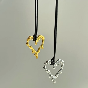 Detail of lava-textured heart pendants in gold and silver on black cords