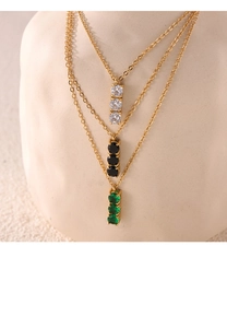 Close-up of gold titanium necklaces with vertical white, black and emerald green zircons
