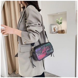 Detail of crossbody camera bag featuring vibrant colorful graffiti print on black leather