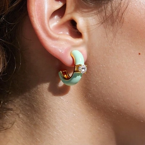 Close-up of a mint green C-shaped earring with a sparkling white zircon on a model
