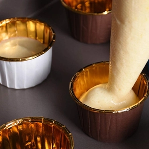 Action shot pouring batter into heat-resistant gold foil-lined cupcake liners