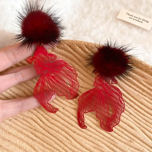 Detailed close-up of hollow carp earrings with red pompom and silver needle studs