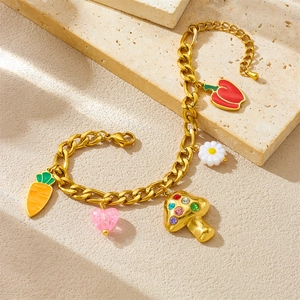 Gold chain bracelet with mushroom, carrot, chili, and daisy charms on a stone surface