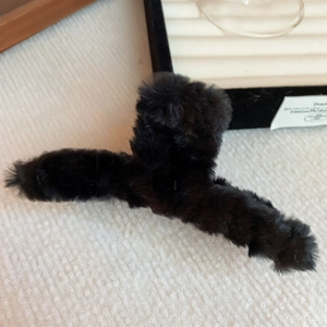Detail of a chic black plush cloud hair claw clip on a light textured fabric background
