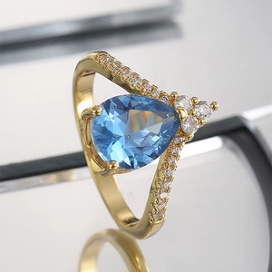Elegant gold pear-cut blue zircon ring with small diamonds on a reflective surface