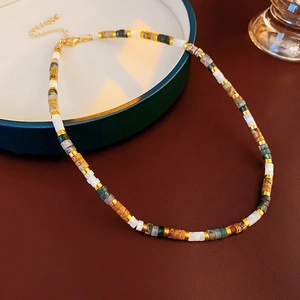 Detail of beaded necklace with white, green and gold beads on dark green tray