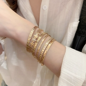 Détail d'un ensemble de bracelets dorés avec fleurs et étoiles, finition polie sur modèle