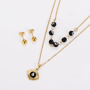 Close-up of golden double-layer necklace with eye pendant and matching ball stud earrings