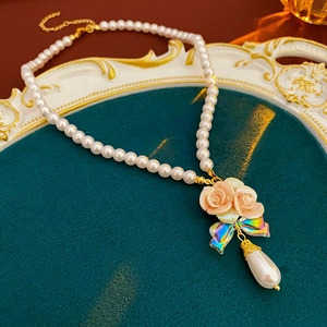 Detail of pink rose and bow pendant with pearl drop on elegant gold-tone pearl necklace