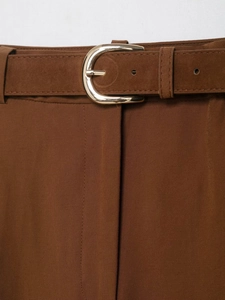 Détail d'une ceinture en daim marron avec boucle en U dorée sur un pantalon de tailleur