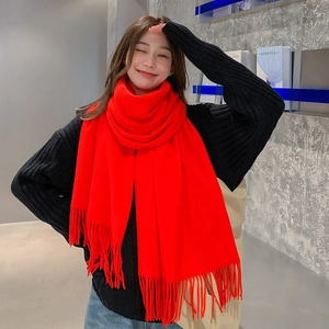 Close-up of a soft red wool-like scarf with fringe detail worn by a smiling model