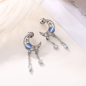 Detail of silver crescent moon earrings with blue stones and dangling rhinestone chains