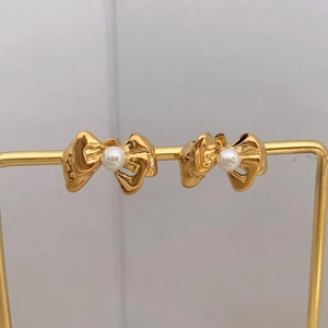 Macro detail of golden bow earrings featuring a white pearl on a metal display