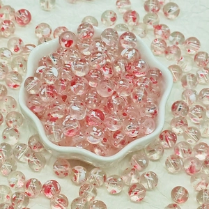 Close-up of translucent round glass beads with red swirl patterns in a petal-shaped bowl