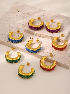 Close-up of C-shaped gold-plated earrings with colorful crystal stones on stone surface