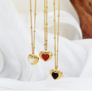 Detailed view of three heart necklaces in black, red and white on gold beaded chains
