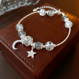 Detail of silver star and moon charms on crystal beaded bracelet over leather