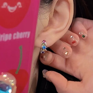 Macro shot of silver ear hoop set with colorful rainbow zircons worn on the ear