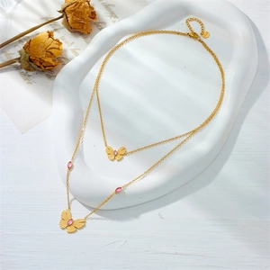 Detail of a double-layered gold butterfly necklace with pink gems on a white tray