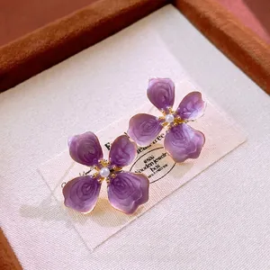 Elegant purple flower enamel earrings with white pearls and gold accents on a display box