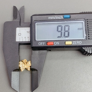 Detailed measurement of gold butterfly pendant showing 9.8mm size on digital caliper
