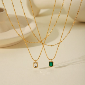 Close-up of double layer gold ball chain necklace with green and clear zircon pendants