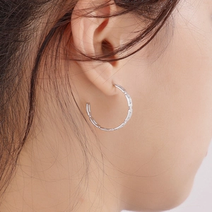 Close-up of silver chain-link C-shaped hoop earrings worn to show elegant metallic texture