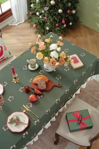 Detailed view of green Christmas tablecloth with white ruffles and holiday embroidery