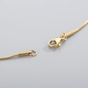 Macro detail of golden lobster clasp and adjustable ring end on a sleek snake chain