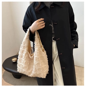 Detail showing the textured fringe fabric and 3D plaid pattern of the cream tote bag