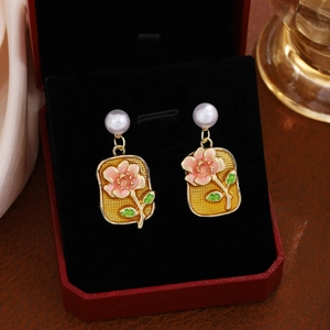 Detailed macro view of pink enamel flower earrings with pearl on a black velvet display