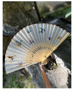 Detail of light blue silk folding fan with butterfly embroidery and tassel on mossy rock