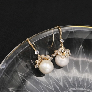 Macro shot of gold pearl earrings with flower zircon details hanging on glass