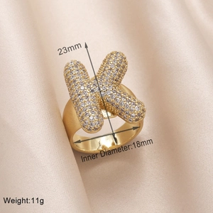 Detailed view of gold-plated letter K ring with cubic zirconia on silk background