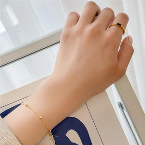 Detail of minimalist gold-plated ring with black zircon and beaded chain bracelet
