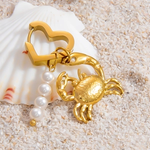 Golden heart earrings with pearl drop and crab pendant on shell background
