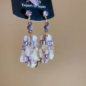 Macro detail of geometric square crystal drop earrings with purple gemstones and gold setting